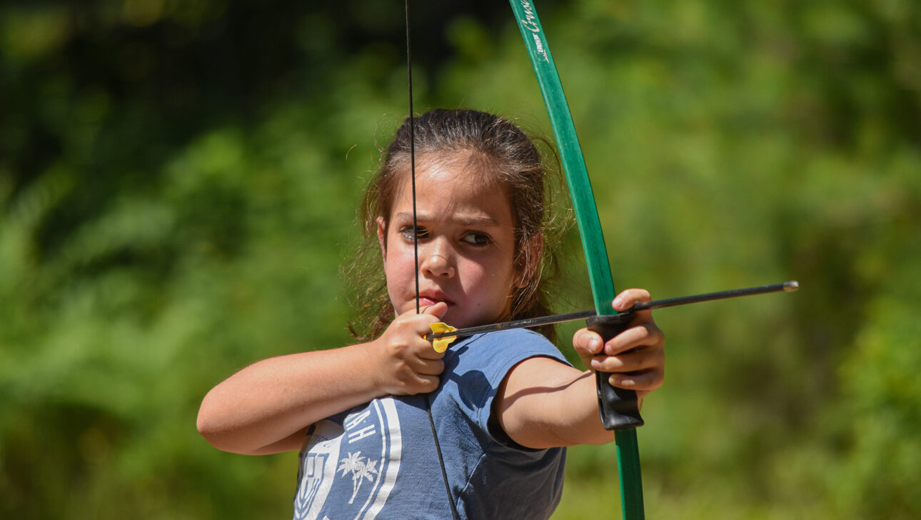 A camper aiming a bow and arrow.