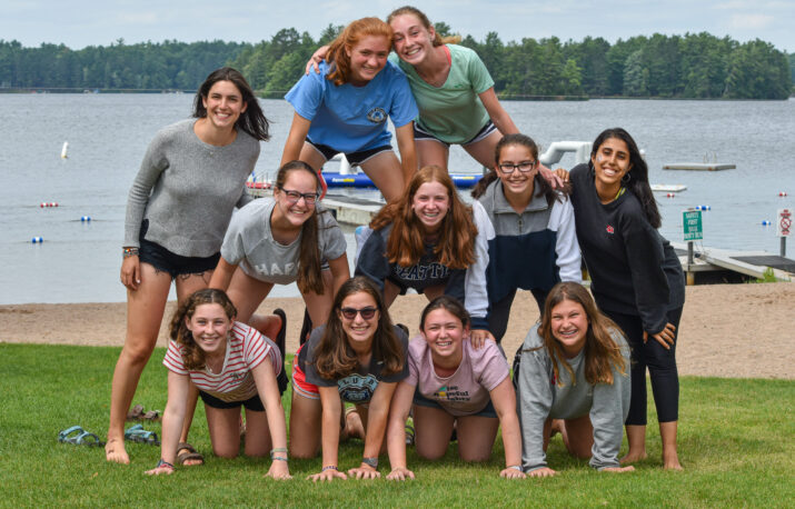 Young women create a pyramid in front of a lake.